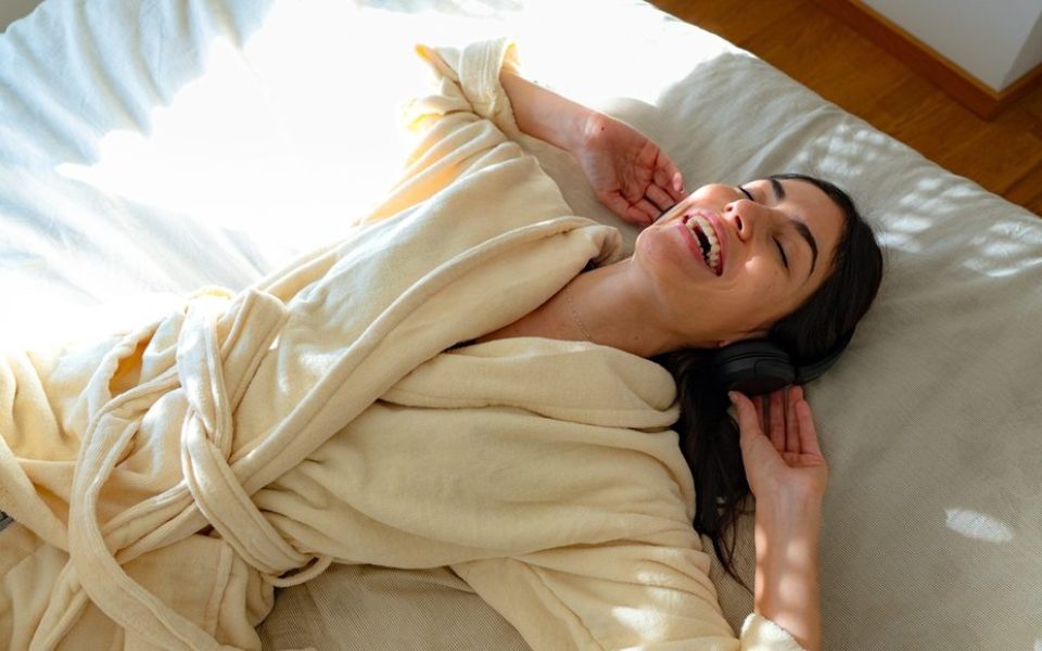 Eine Frau lächelt lustvoll, während sie mit einem Kopfhörer im Bett liegt